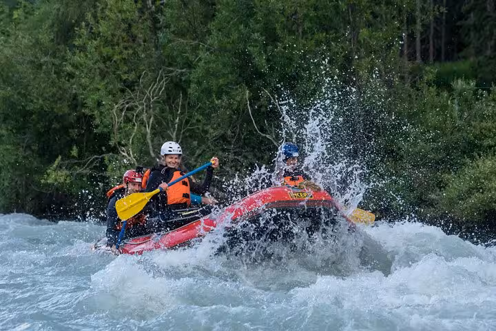 Excited team navigating rough waters in Engadin's whitewater rafting adventure, splashing through waves amidst lush scenery.