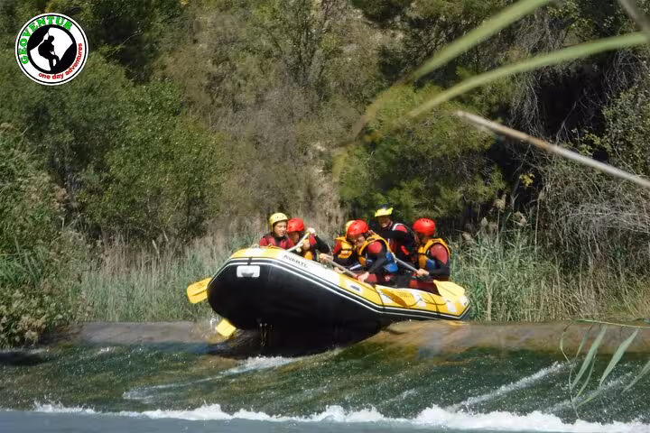 Whitewater rafting in Teruel with helmeted group riding a yellow raft over a small rapid on a scenic river