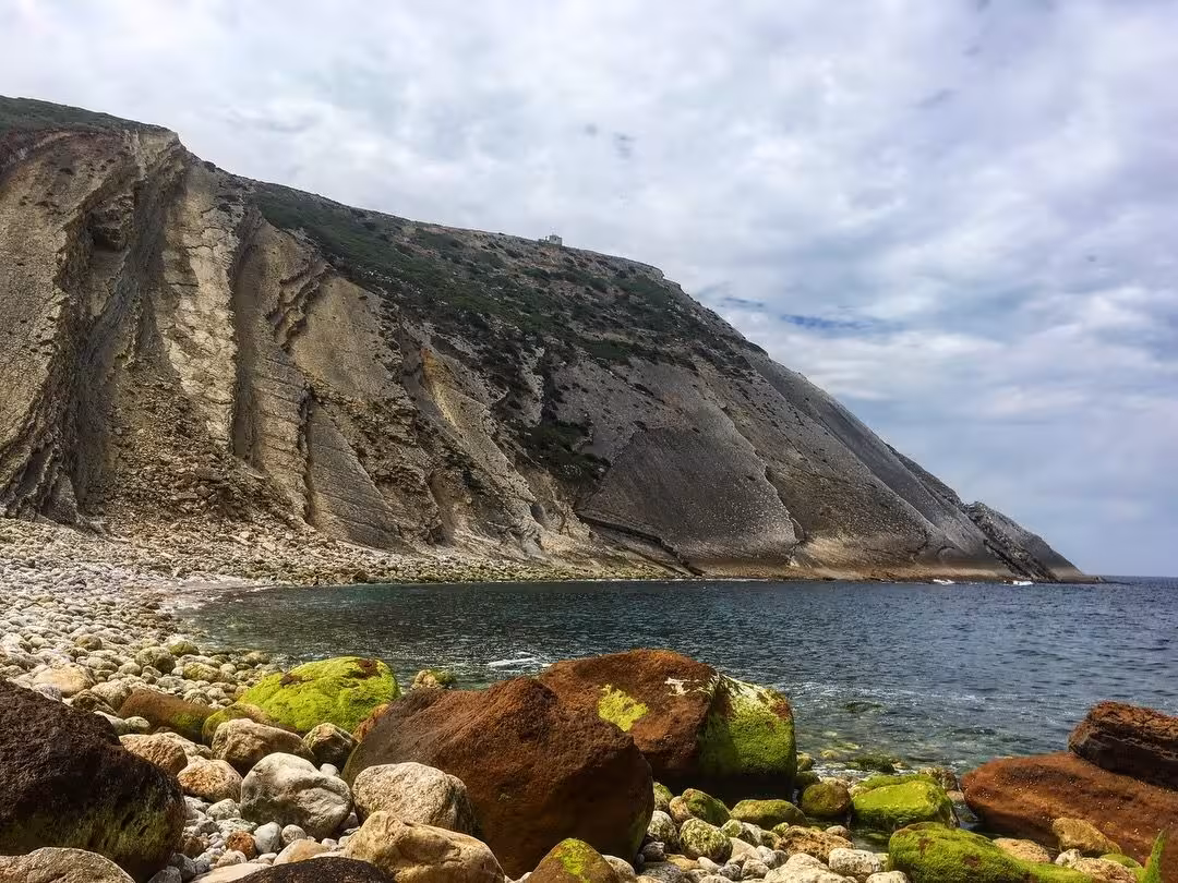 Rocky beach and dramatic sea cliffs on the Hiking Wild West Coast tour, with clear water and mossy boulders