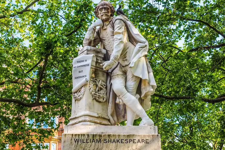 William Shakespeare statue with quote 'There is no darkness but ignorance' surrounded by green trees in London