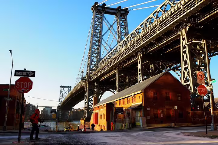 Williamsburg Bridge towering over a brick building at a street corner with stop signs in Brooklyn