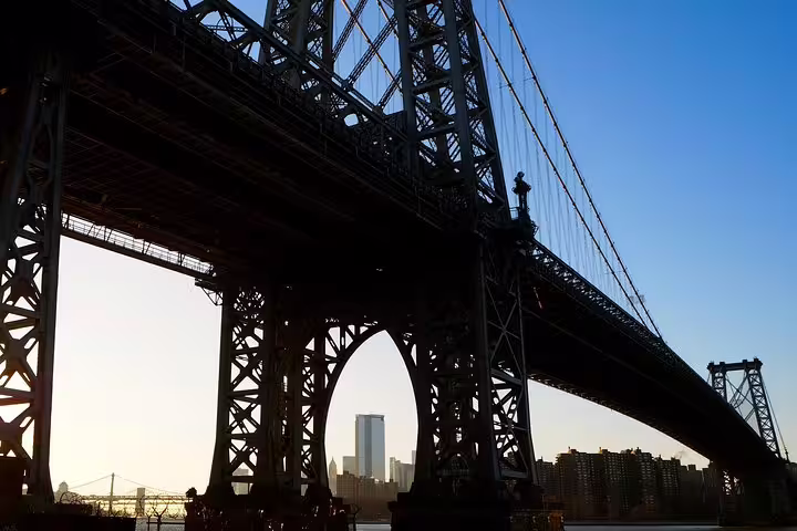 Williamsburg Bridge silhouette at dusk with NYC skyline visible through steel arches