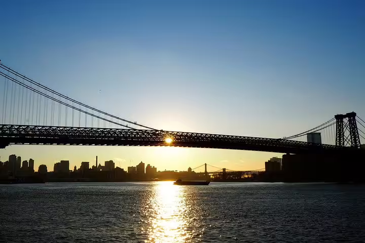 Williamsburg Bridge silhouette at sunset over East River with NYC skyline in background