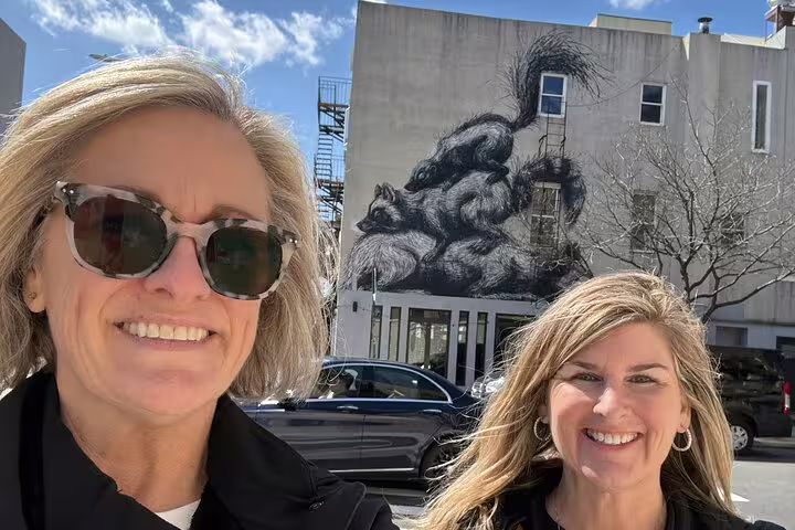 Two smiling women taking a selfie in front of a large squirrel street art mural in Williamsburg Brooklyn
