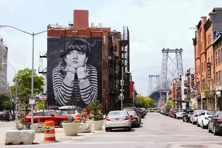 Large black and white street art mural on brick building in Williamsburg Brooklyn with Williamsburg Bridge in background