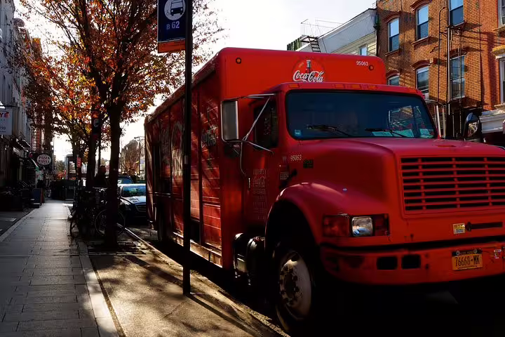 Red Coca-Cola delivery truck parked on a tree-lined street in Williamsburg, Brooklyn