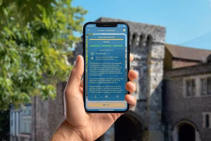 Hand holding phone showing Winchester Westgate quest details on GPS tour app with medieval castle in background