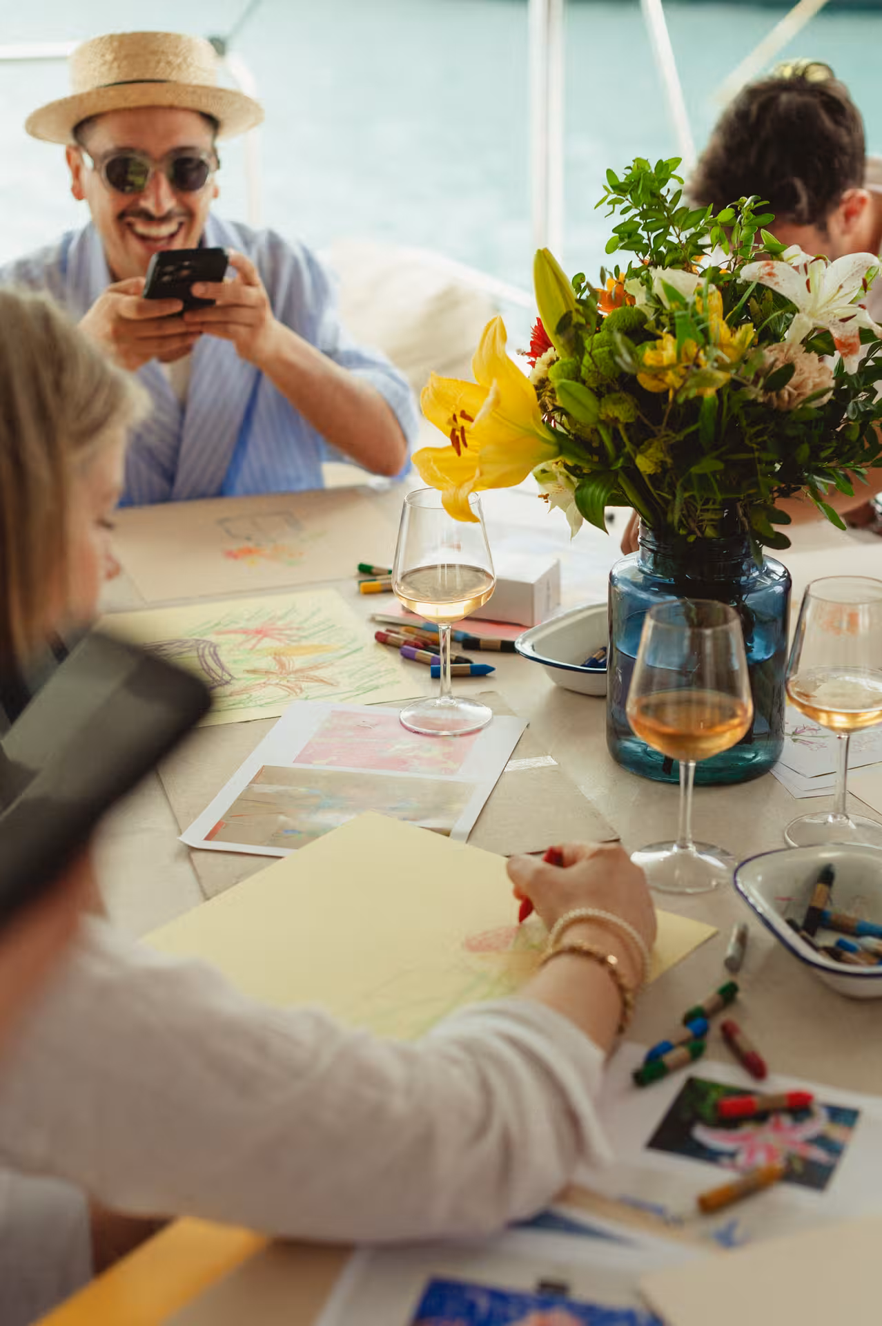 Guests sketch and color at a table with wine glasses and fresh flowers during a Wine & Art workshop cruise