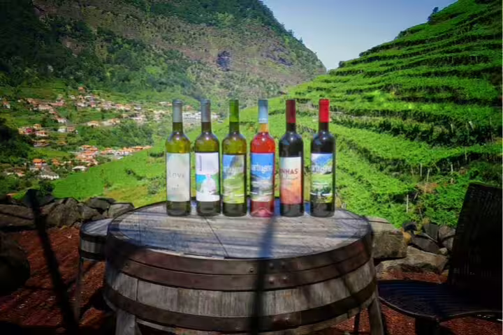 Wine bottles on a barrel table with lush Madeira vineyards and Cabo Girão in the background, showcasing Jeep Safari tour highlights.