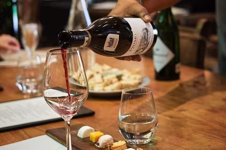 Red wine being poured into a glass, accompanied by a cheese platter, in a cozy wine tasting setting.