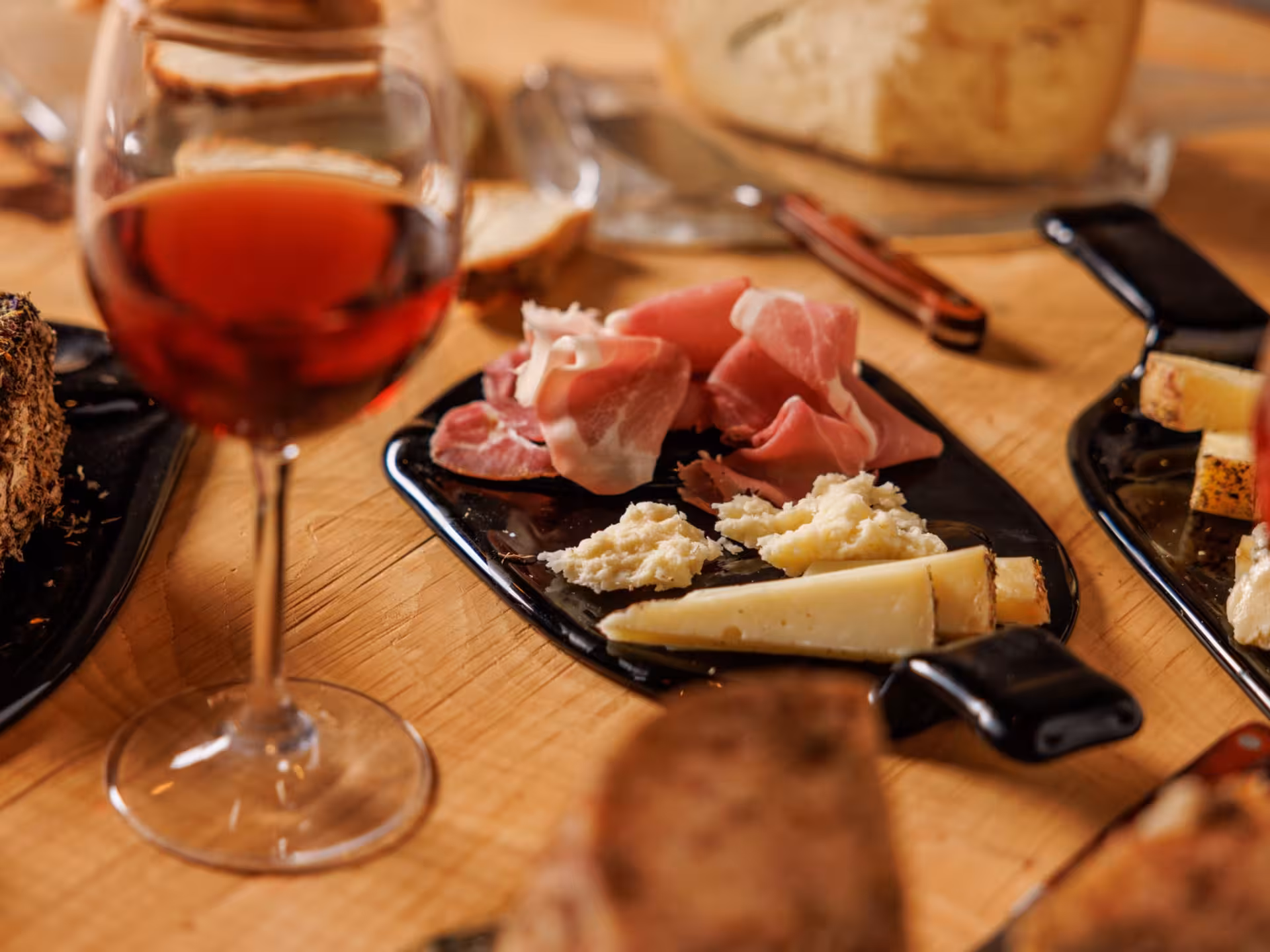 Close-up of wine glass and charcuterie platter with cheese and prosciutto in an underground cellar in Rome.