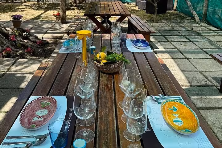 Rustic outdoor table set for a wine pairing lunch with colorful plates and lemons in Sorrento's lemon grove.