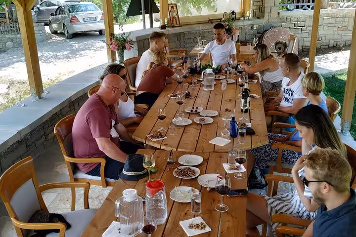 Guests enjoying a wine tasting session in Berat, seated at a long wooden table under a shaded patio.