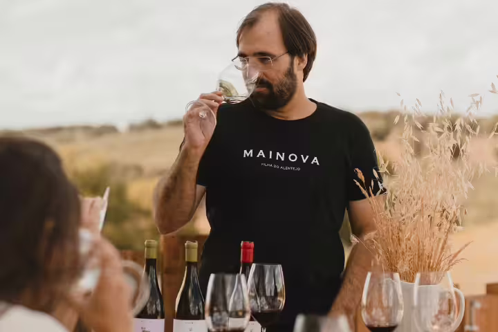 A wine expert tastes a selection of six wines outdoors, surrounded by bottles and glasses, enhancing the vineyard experience.