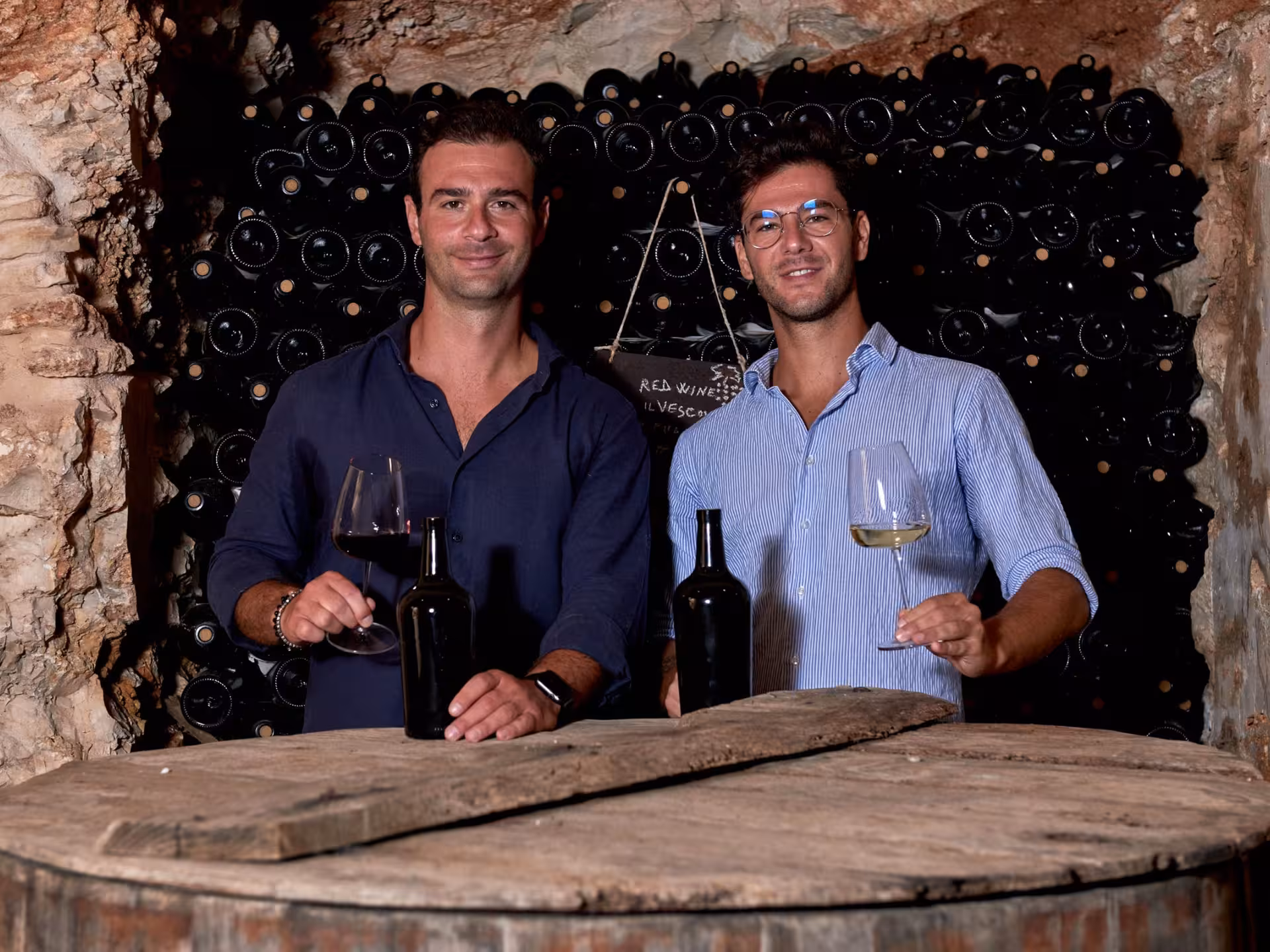 Two men in a wine cellar showcasing red and white wines during a tasting experience in Bari City Center.