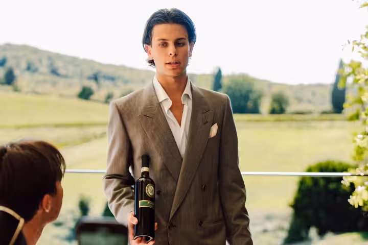 Sommelier presenting red wine bottle at outdoor Tuscan dining table with vineyard views