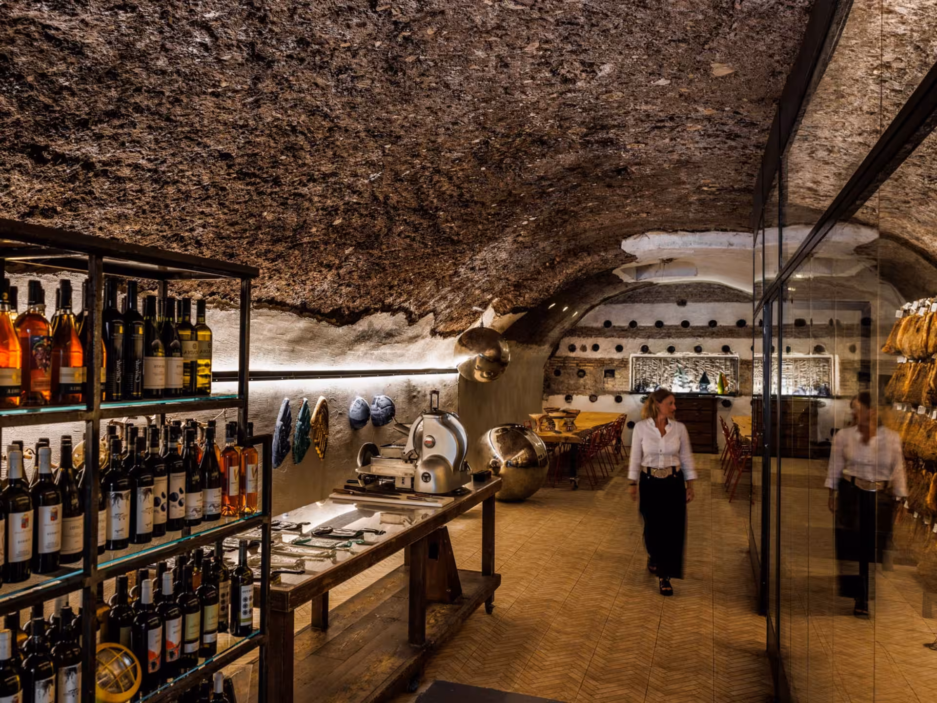 Underground wine cellar in Rome featuring wine racks, a meat slicer, and dining area, perfect for wine tasting tours.