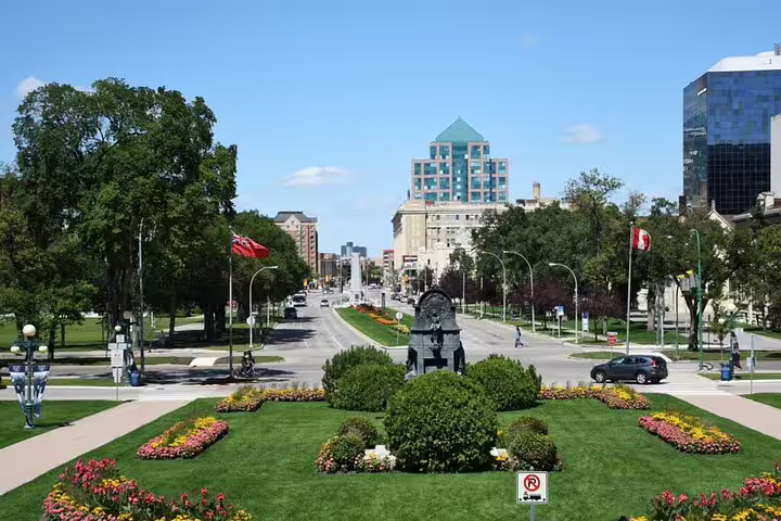Scenic view of Memorial Boulevard in Winnipeg with flower gardens, monuments, and downtown buildings