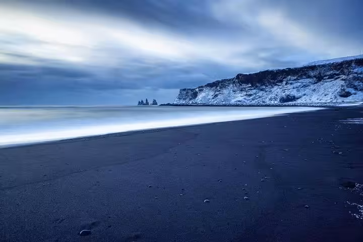 Black sand beach with snow-dusted cliffs and sea stacks along Iceland's south coast in winter