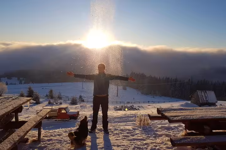 Hiker with arms outstretched in snowy winter landscape at sunrise near Vladeasa Peak Apuseni