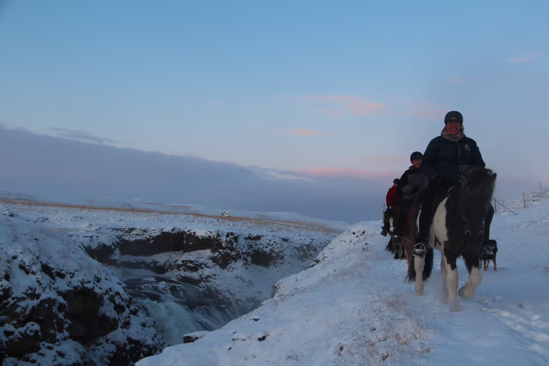 Riders on horseback along snowy canyon edge near waterfall at dusk in Skagafjordur Iceland