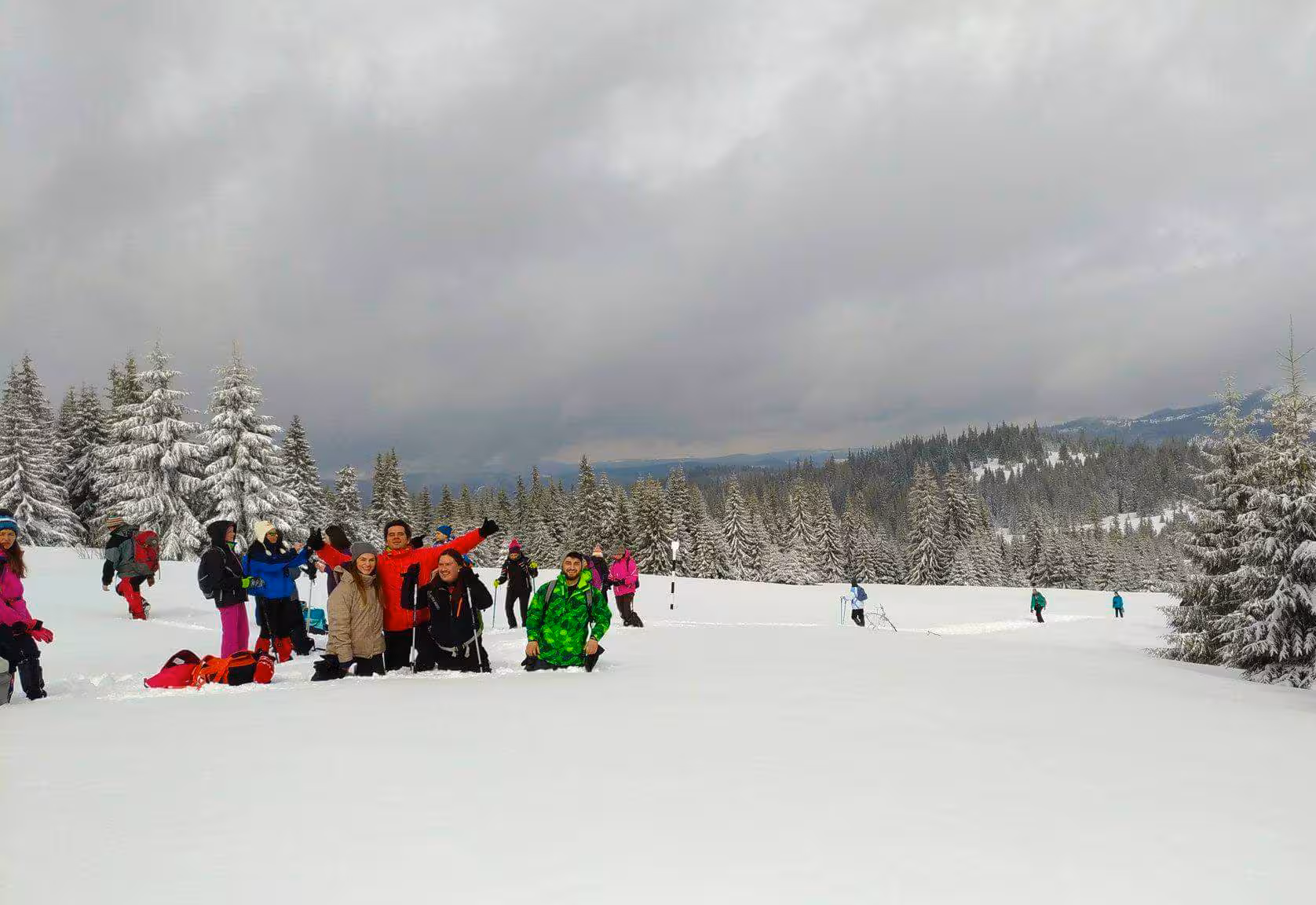 Group of hikers with snowshoes posing on snowy mountain trail surrounded by snow-covered pine trees in winter