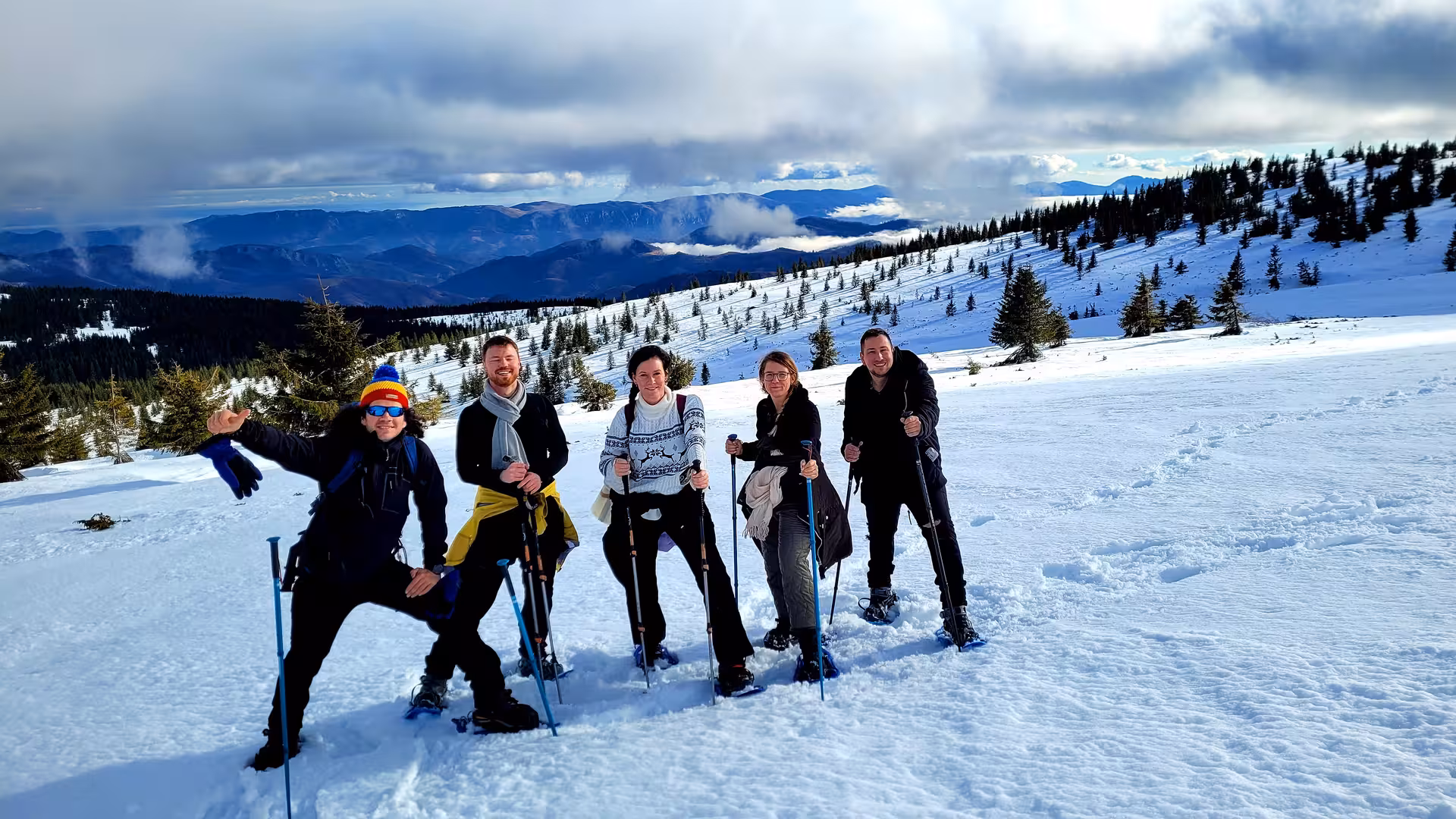 Group of five hikers with trekking poles snowshoeing on a snowy mountain slope near Cluj-Napoca