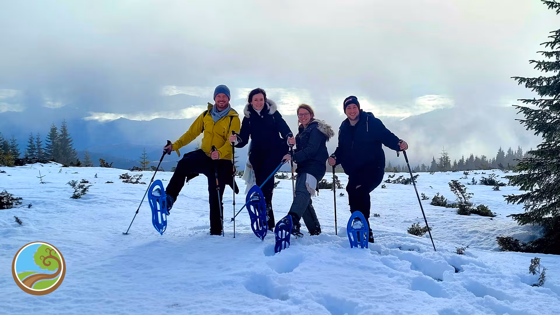 Four smiling hikers with blue snowshoes and trekking poles on a snowy mountain near Cluj-Napoca