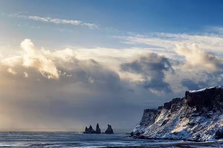 Snow-covered cliffs and black sand beach with dramatic sea stacks rising from the ocean in winter Iceland