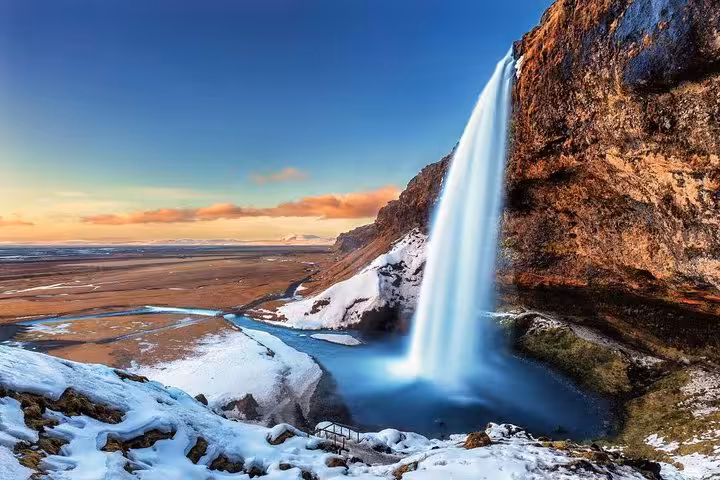Seljalandsfoss waterfall cascading over snow-covered cliffs in winter with Icelandic plains in the background