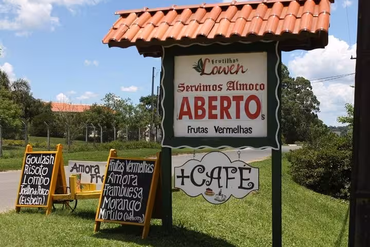 Entrance sign for a café in Witmarsum Colony, Paraná, showcasing German culinary offerings and local fruits.