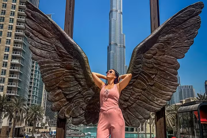 Woman posing with angel wings sculpture in front of Burj Khalifa during Dubai Layover Instagram Videography Tour.