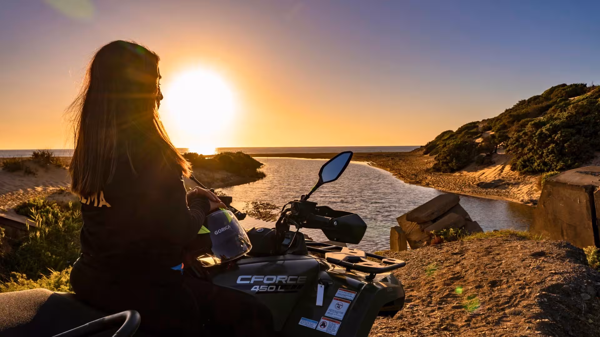 Woman on ATV enjoying a stunning sunset view over Arbus dunes and river, perfect for adventure seekers.