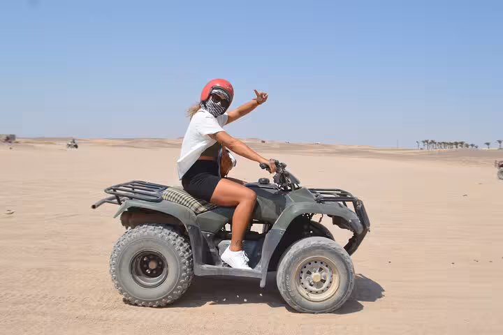 Woman riding ATV quad bike across Sharm El-Sheikh desert sands, part of sunset safari with BBQ dinner show