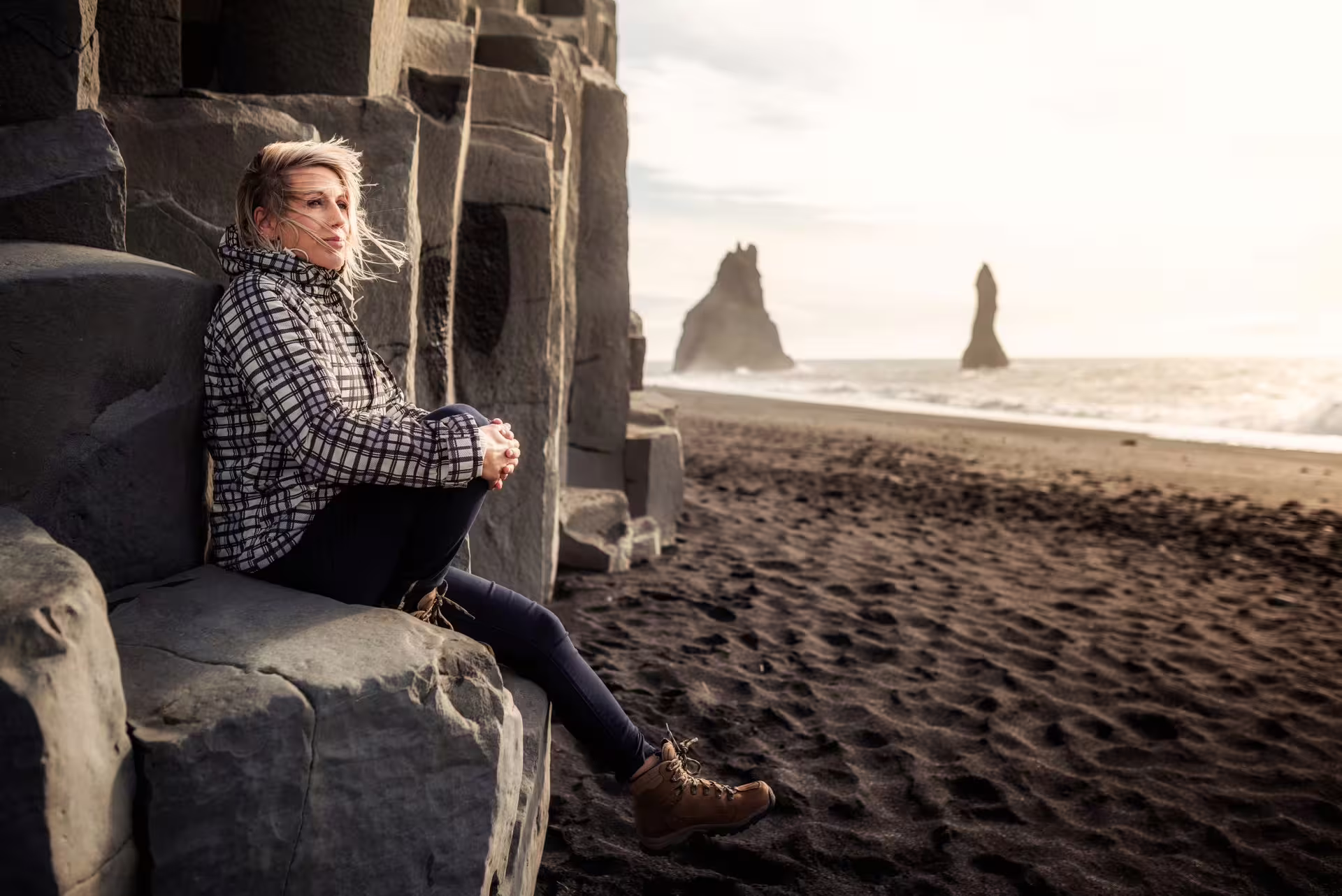 Woman resting on basalt columns at Reynisfjara black sand beach with sea stacks on Iceland South Coast private tour