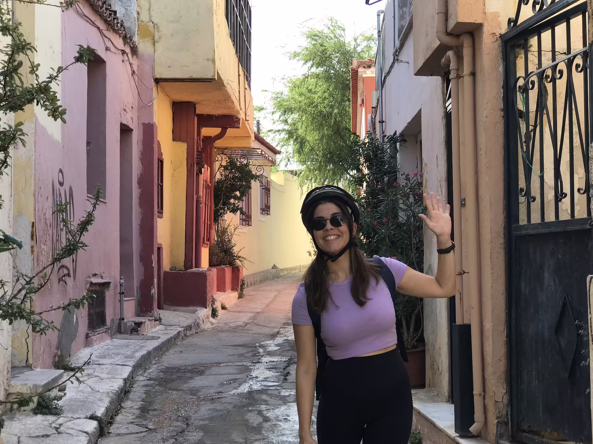 A woman waves while enjoying a bike tour through the colorful, charming streets of Athens' historical neighborhoods.