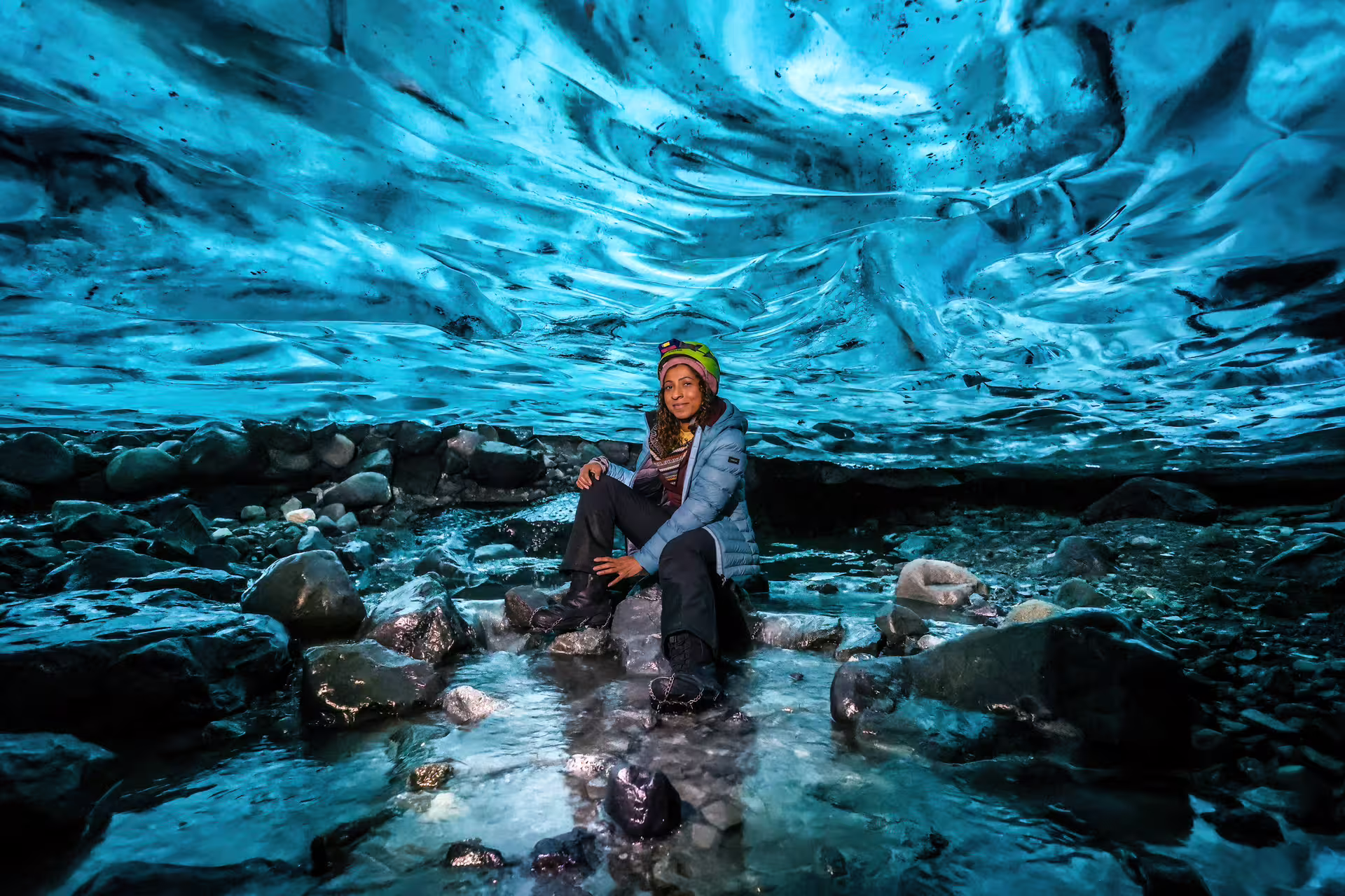 Woman sitting on rocks inside a stunning blue crystal ice cave on Vatnajokull Glacier Iceland tour