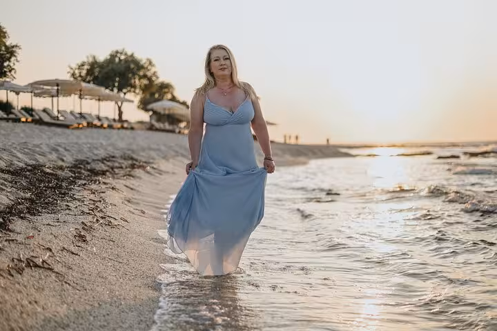 Woman in blue dress walking along the shoreline at Anisaras beach during a serene sunset photoshoot.