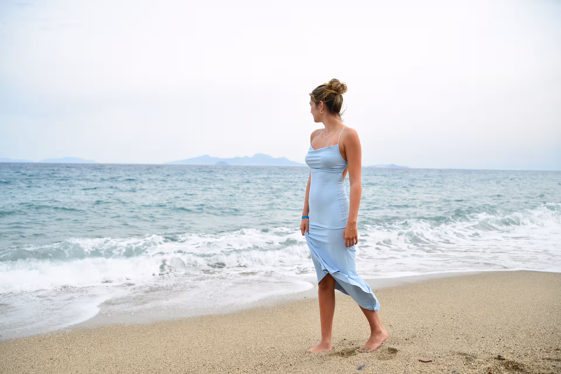 Woman in blue dress gazing at the sea on Heraklion Venetian Port beach, capturing a serene photoshoot moment.