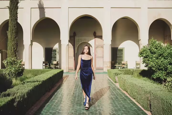 Woman in blue dress walking through lush garden at historic Marrakesh palace, showcasing Moroccan architecture.