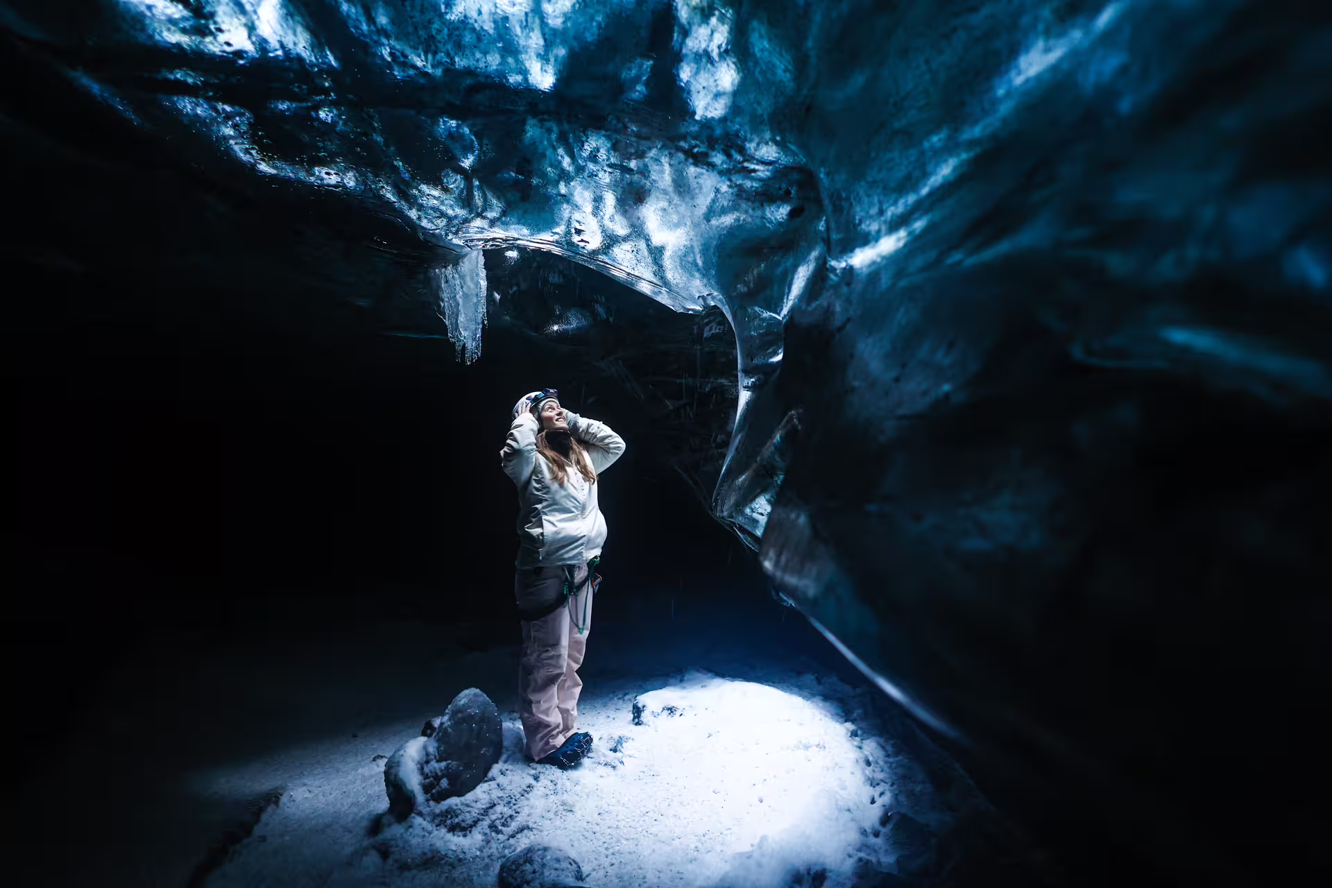 A woman in winter gear marvels at the breathtaking blue ice walls deep inside an Iceland glacier ice cave tour.