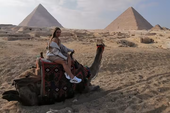 Woman on camel with Giza Pyramids backdrop on Cairo camel ride and lunch with quad bike and shopping tour