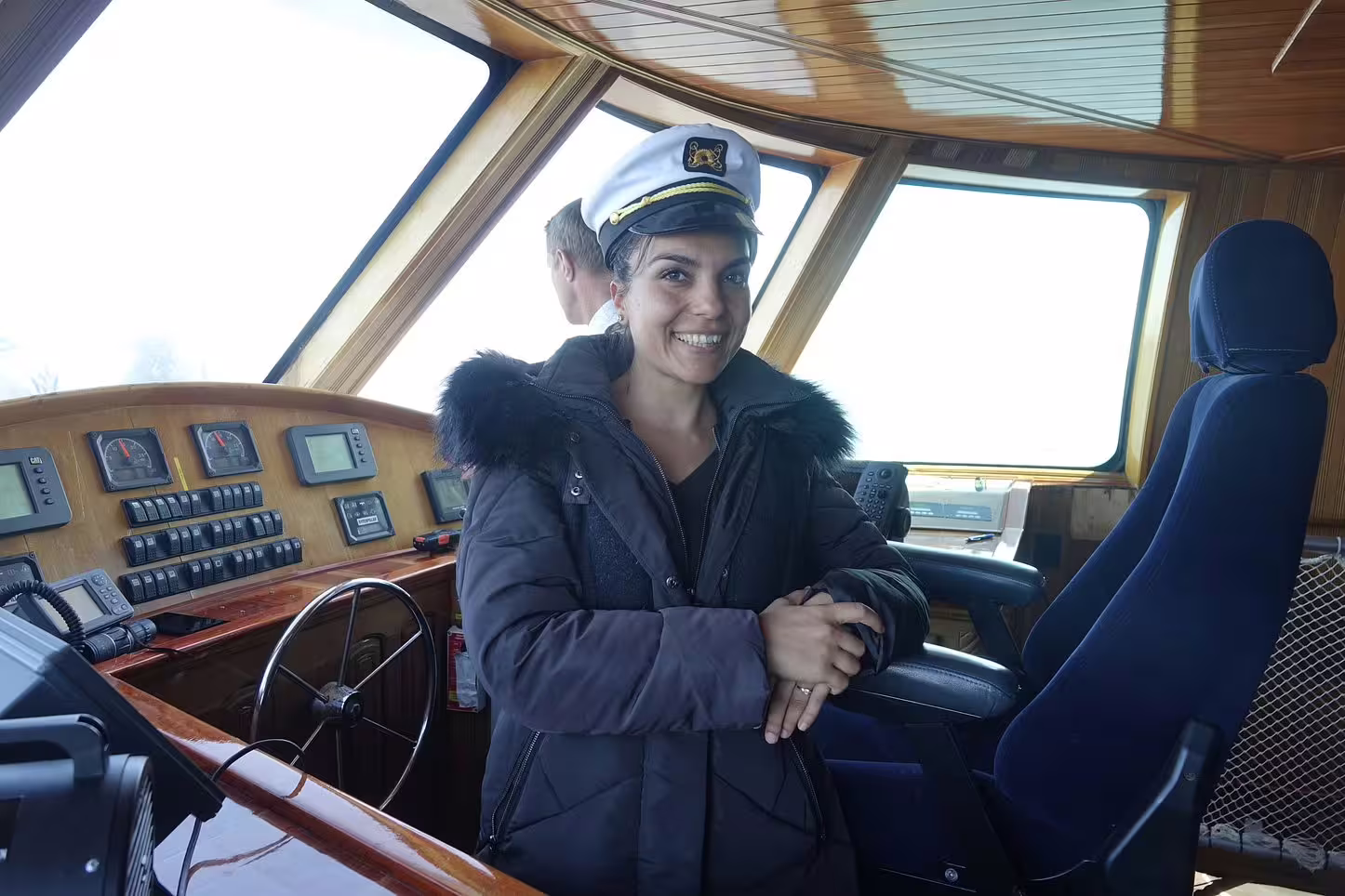 Smiling woman wearing captain's hat on yacht bridge with navigation controls in Reykjavik