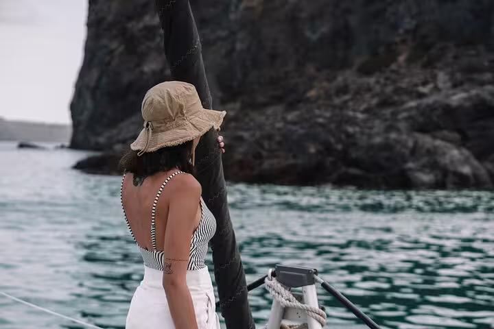 Woman in a sun hat enjoying scenic views on a private catamaran cruise in Santorini's crystal-clear waters.