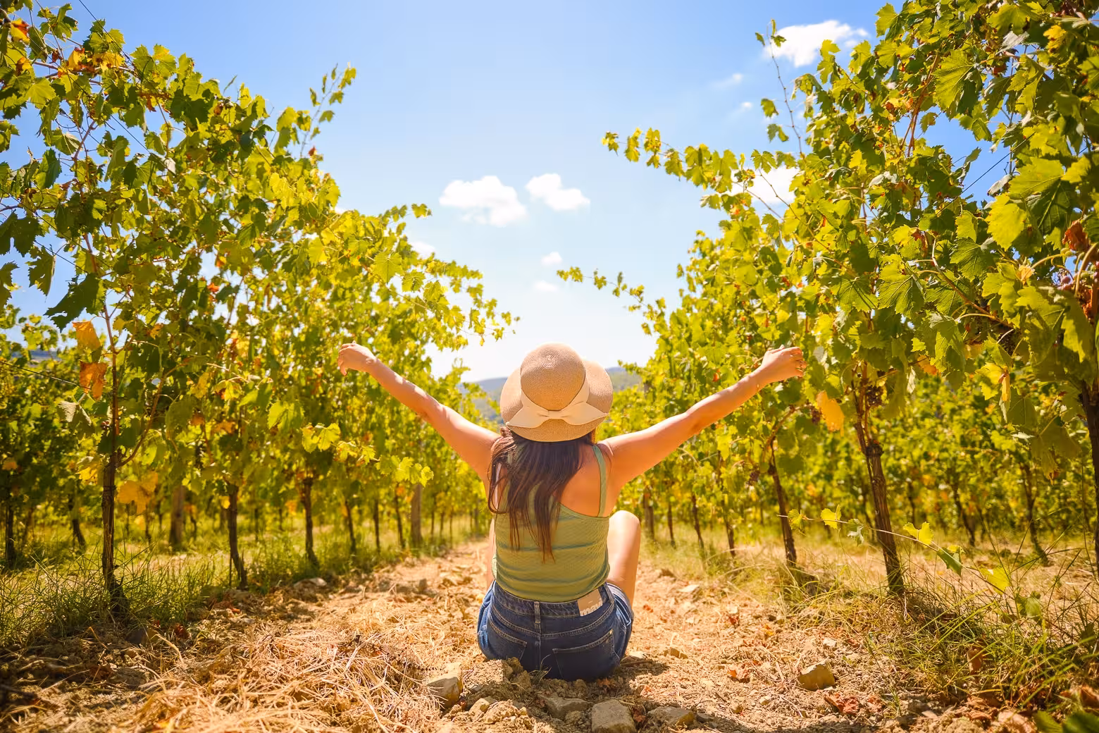 Woman enjoying the Chianti vineyard, arms raised in celebration under the bright Tuscan sky.