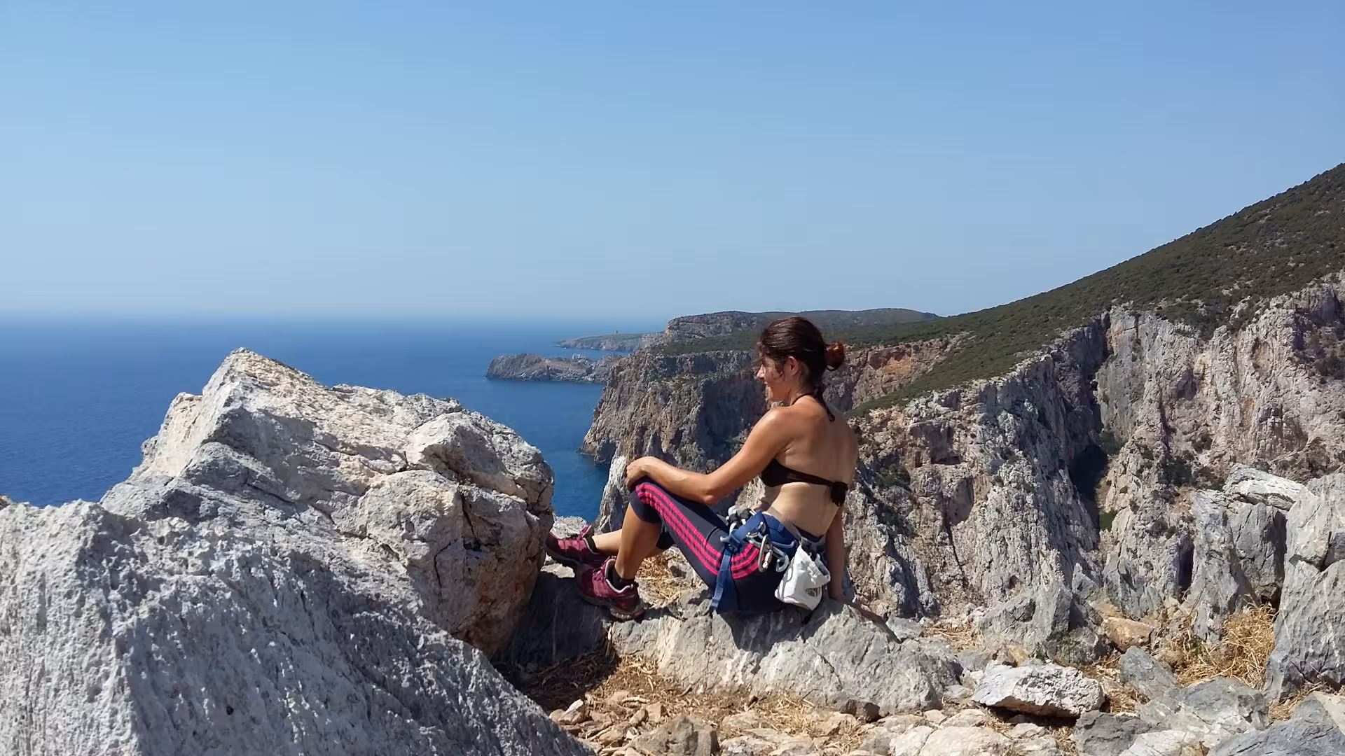 Woman resting on rocky cliff with panoramic sea view during Pan di Zucchero climbing tour from Masua.