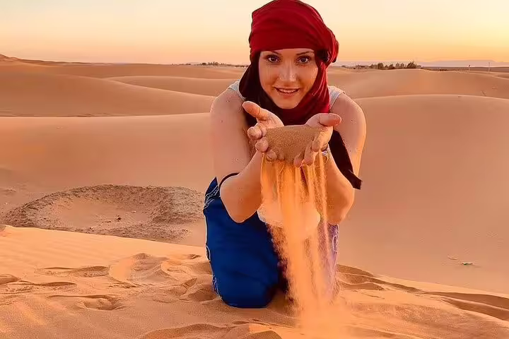 Woman holding flowing sand on Erg Chebbi dunes in Merzouga during 3 days desert tour from Fes to Marrakech