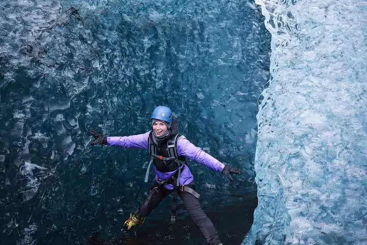 Happy female adventurer exploring stunning blue ice cave on guided glacier adventure tour from Glacier Lagoon