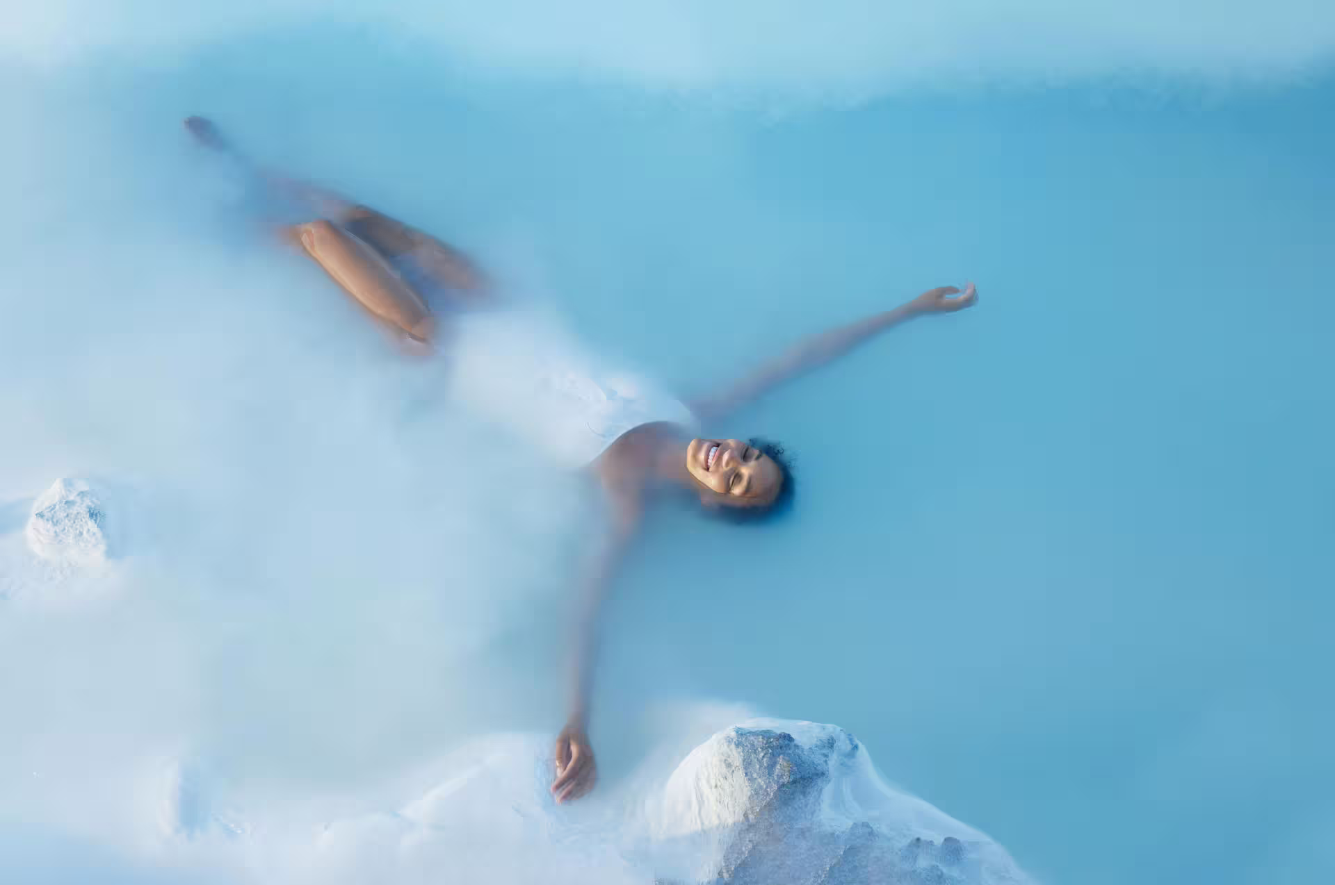 Woman floating and smiling in the milky blue geothermal waters of Blue Lagoon Iceland