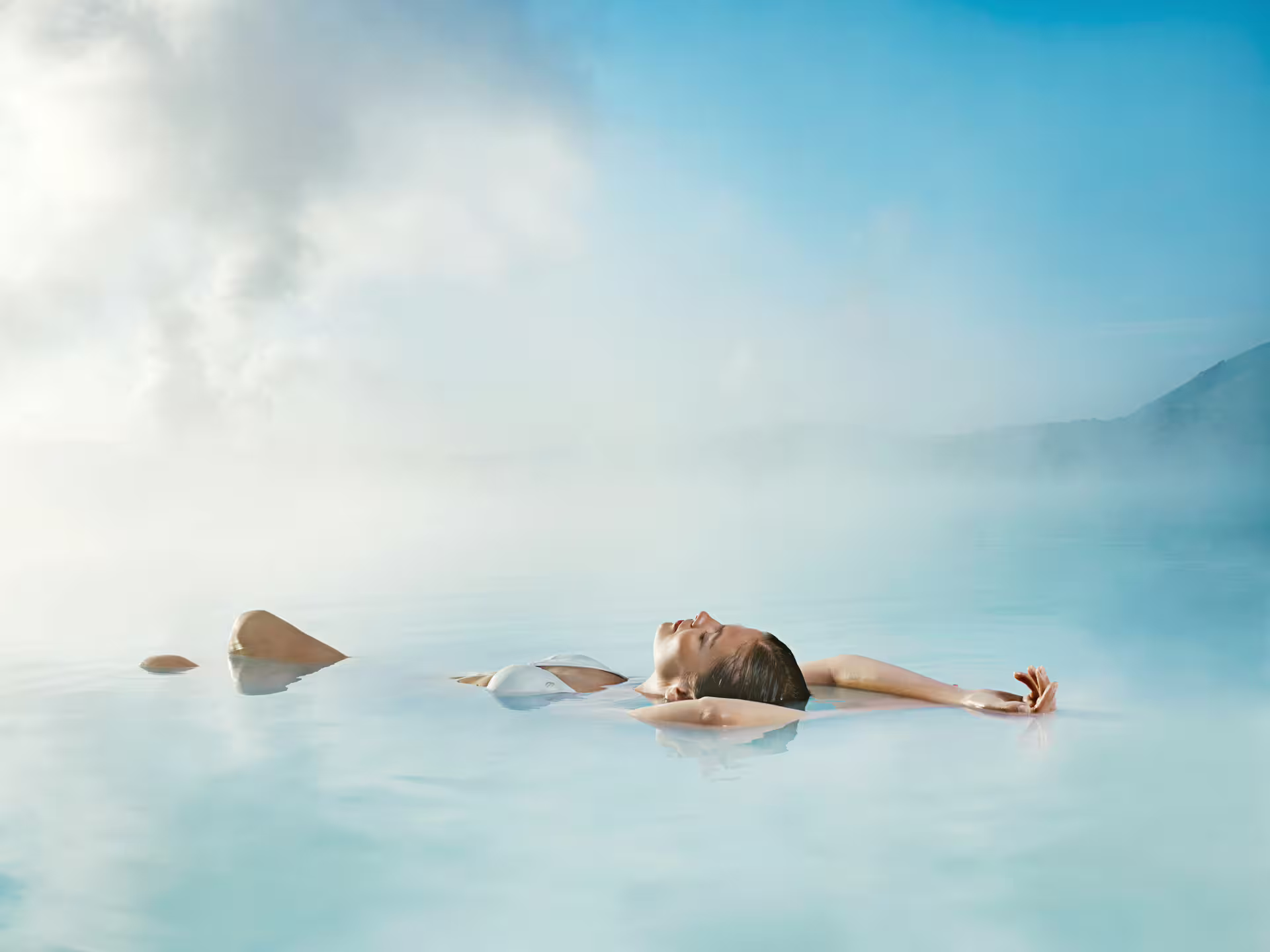 Woman floating peacefully in the steamy turquoise waters of Iceland's Blue Lagoon geothermal spa